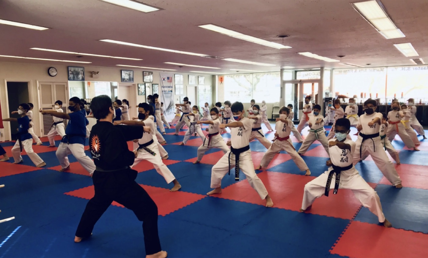 A large group of children in white uniforms practicing punches together on a red and blue mat