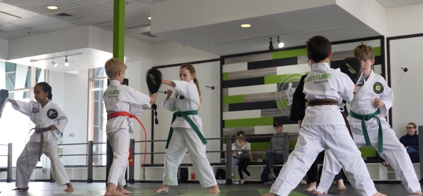 A student practicing a punching drill on focus pads with a partner holding the pads